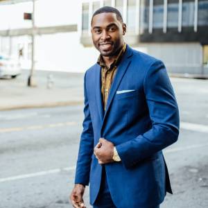 Man in blue suite standing beside a street smiling at the camera